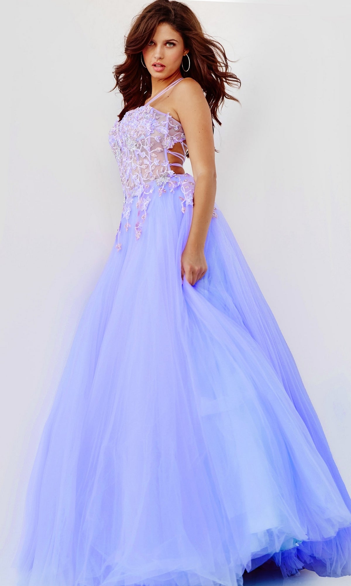A woman poses against a plain light background in the Lilac Purple Sheer-Bodice Prom Ball Gown by Jovani, featuring a tulle skirt and floral embroidery.